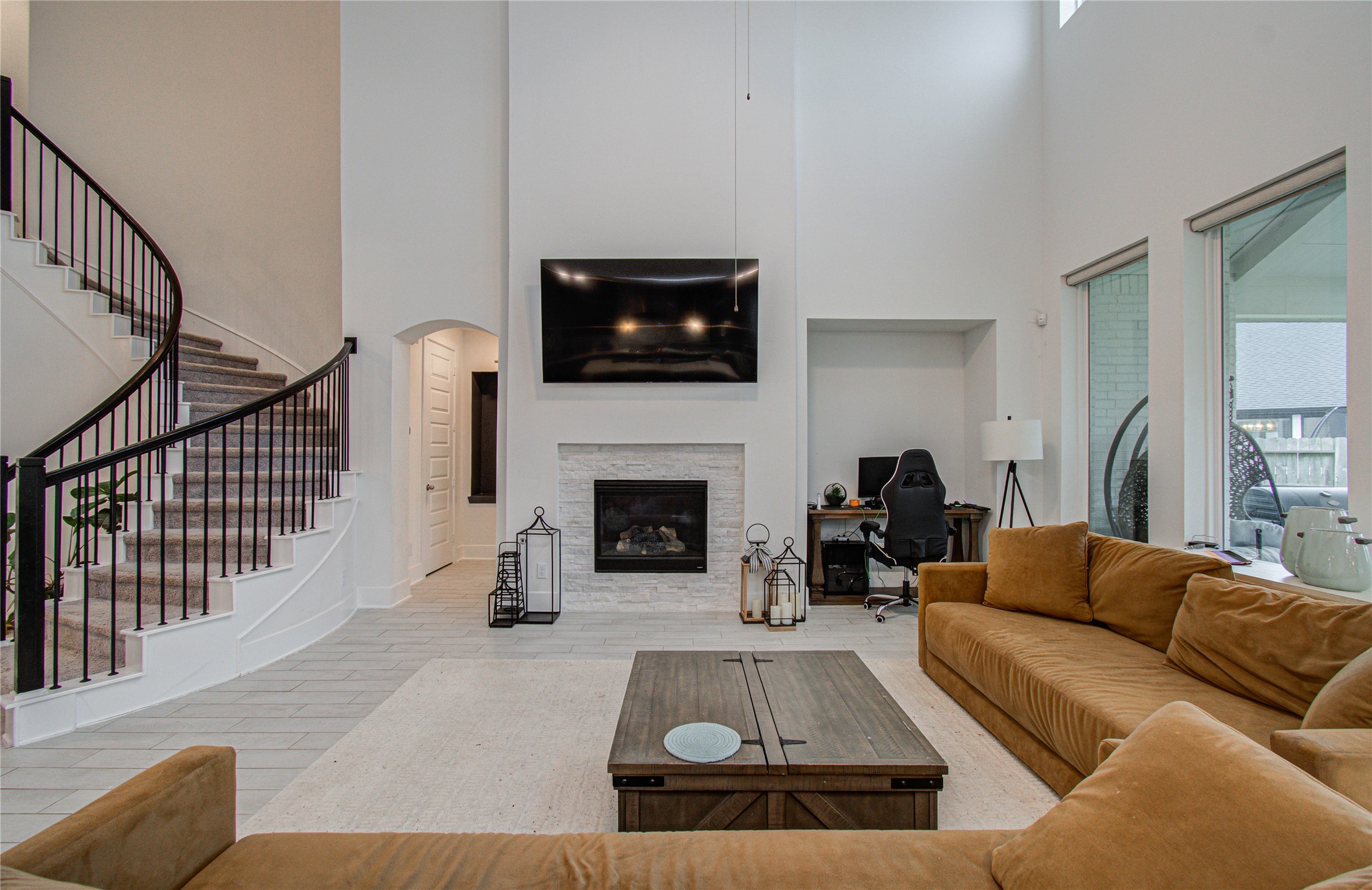 4211 Limestone Terrace Manvel, TX 77578 - Photo 14 of 33 This spacious living room features high ceilings and a modern design with a cozy fireplace, large TV, and a stylish curved staircase. Abundant natural light floods the space through large windows, and there's an adjacent office nook for convenience.