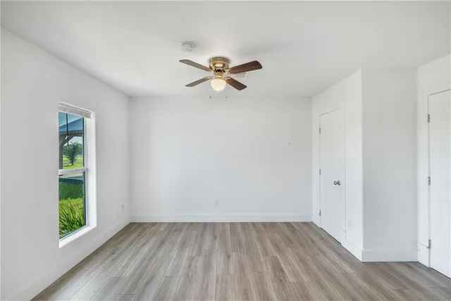an empty room with wooden floor fan and windows