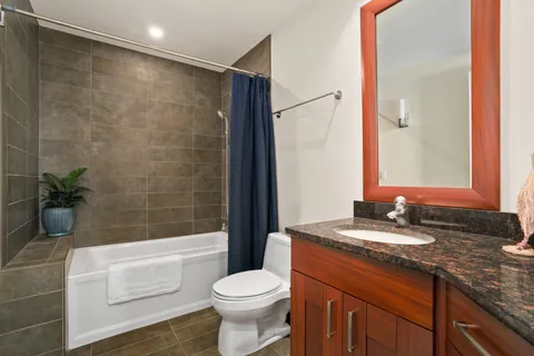 a bathroom with a granite countertop sink a toilet a mirror a bathtub and shower
