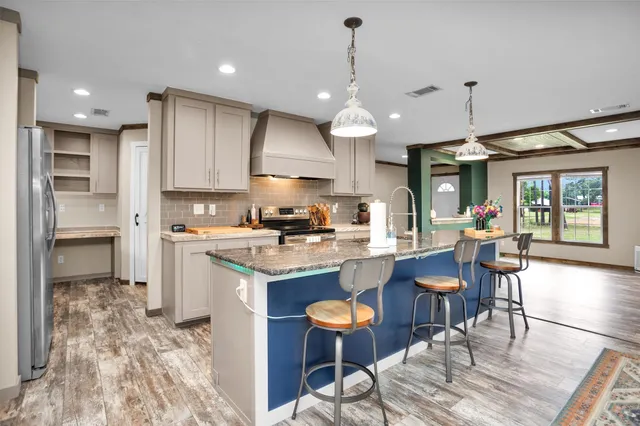 a kitchen with stainless steel appliances kitchen island granite countertop a stove a sink a refrigerator and a dining table with wooden floor