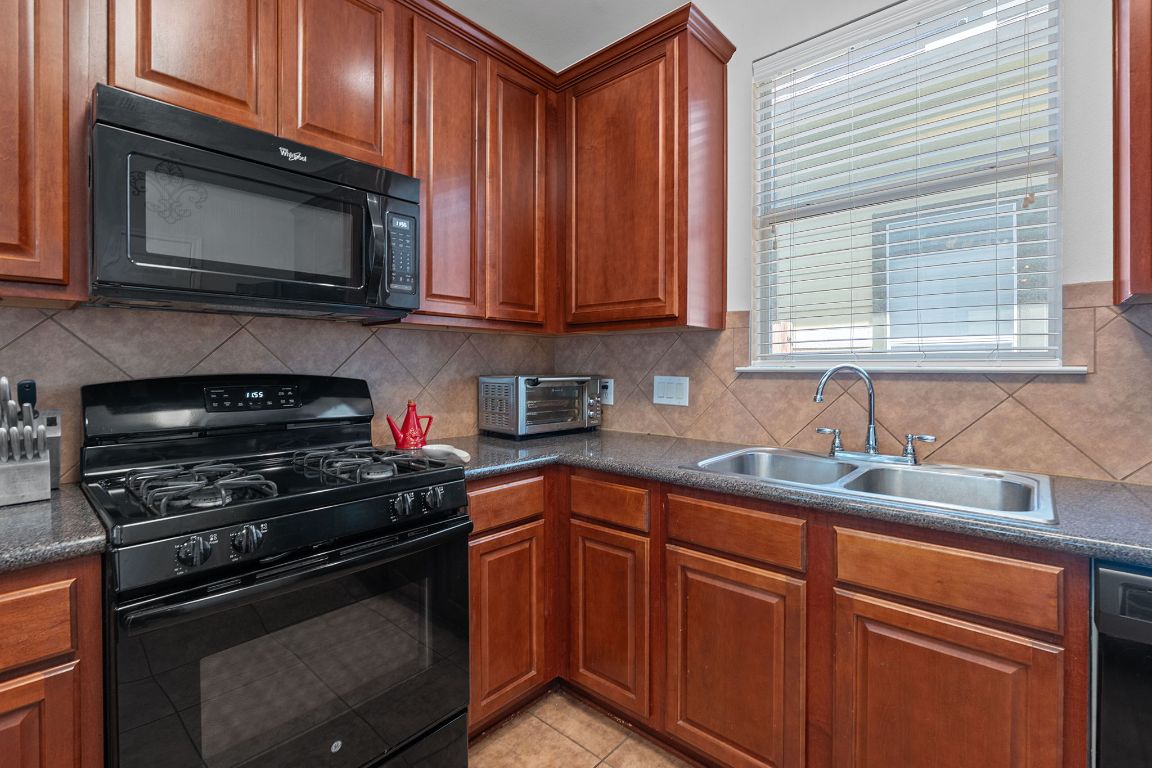 10700 Macmora Road, Unit 116 Austin, TX 78758 - Photo 11 of 26 Kitchen featuring black appliances, decorative backsplash, light tile patterned floors, and brown cabinetry