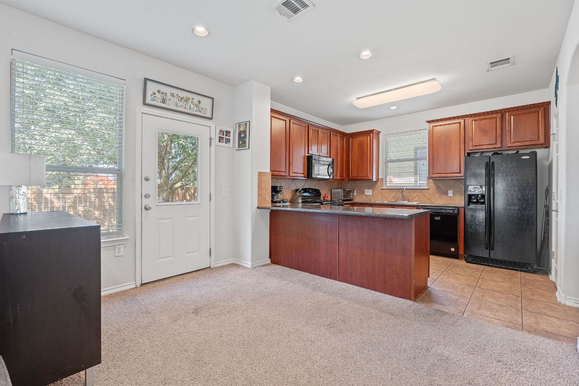 10700 Macmora Road, Unit 116 Austin, TX 78758 - Photo 6 of 26 Kitchen featuring light colored carpet, black appliances, tasteful backsplash, brown cabinetry, and recessed lighting