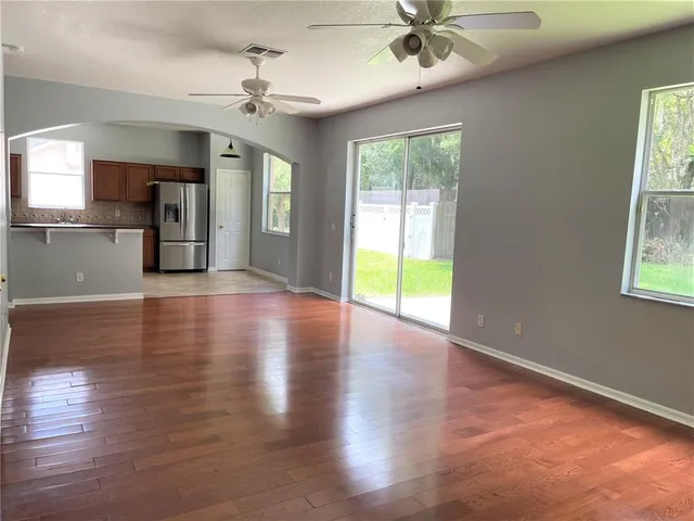 a view of a livingroom with wooden floor a ceiling fan and windows