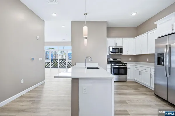 a kitchen with stainless steel appliances kitchen island granite countertop a refrigerator a sink a stove and white cabinets with wooden floor