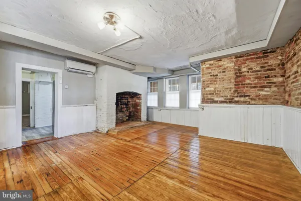 a view of an empty room with wooden floor fireplace and a window