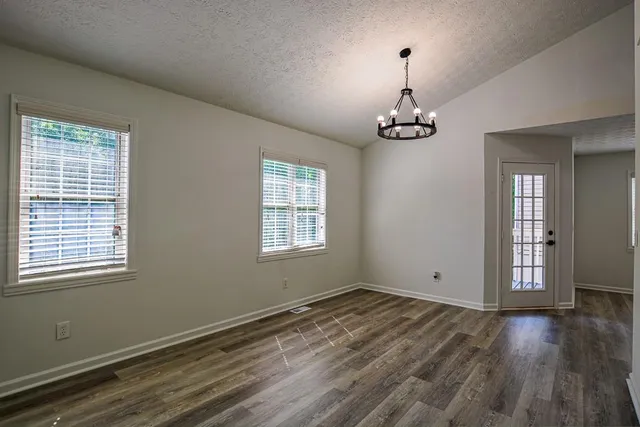 an empty room with wooden floor chandelier fan and windows