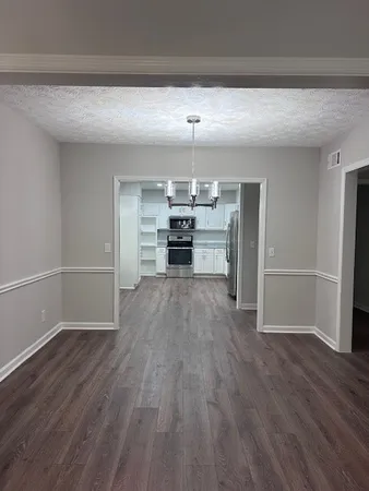 an empty room with wooden floor kitchen view and windows