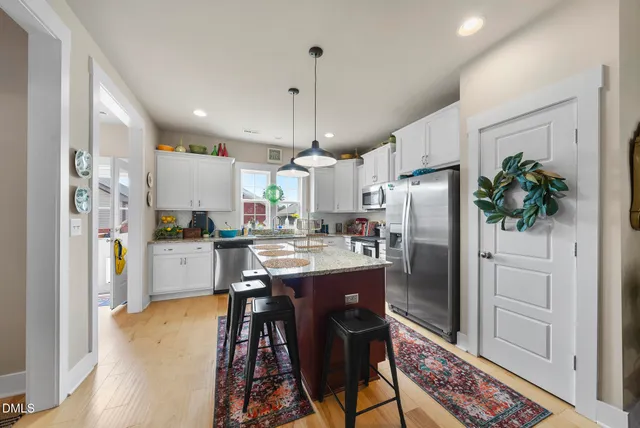 a kitchen with stainless steel appliances granite countertop a refrigerator a sink dishwasher a stove and a dining table with wooden floor