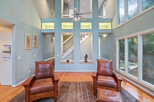 a living room with furniture two large window and wooden floor