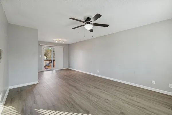 a view of an empty room with wooden floor and a ceiling fan