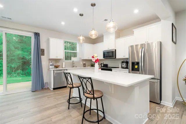 a kitchen with stainless steel appliances a refrigerator a stove a sink dishwasher a dining table and chairs with wooden floor