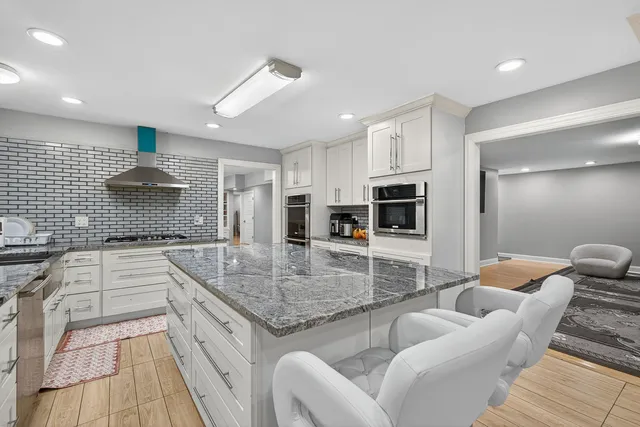 a kitchen with stainless steel appliances granite countertop a stove top oven a sink dishwasher a dining table and chairs with wooden floor