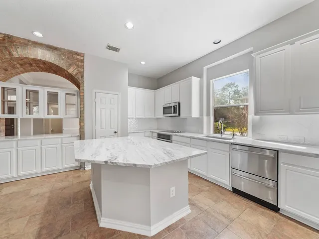 a large white kitchen with kitchen island a sink stainless steel appliances and cabinets