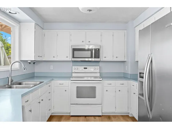 a kitchen with stainless steel appliances granite countertop a sink a stove a refrigerator and white cabinets