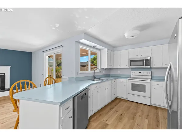 a kitchen with stainless steel appliances granite countertop a stove a sink dishwasher a microwave oven and a dining table with wooden floor