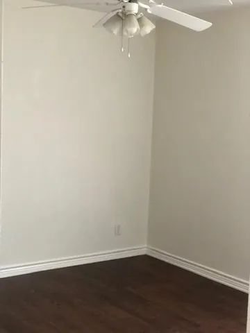 a view of an empty room with wooden floor and fan