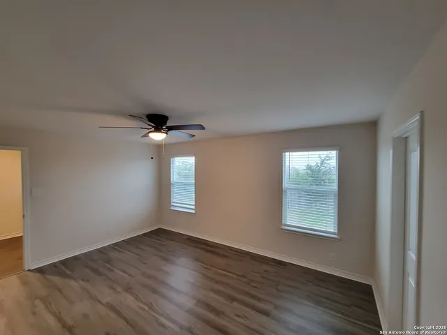 an empty room with wooden floor chandelier fan and windows