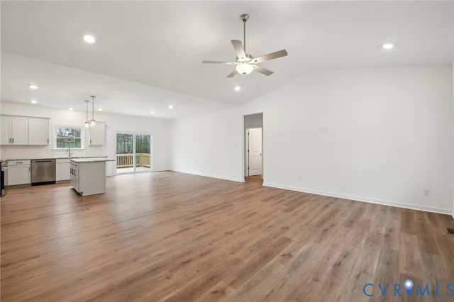 an empty room with wooden floor kitchen appliances and windows
