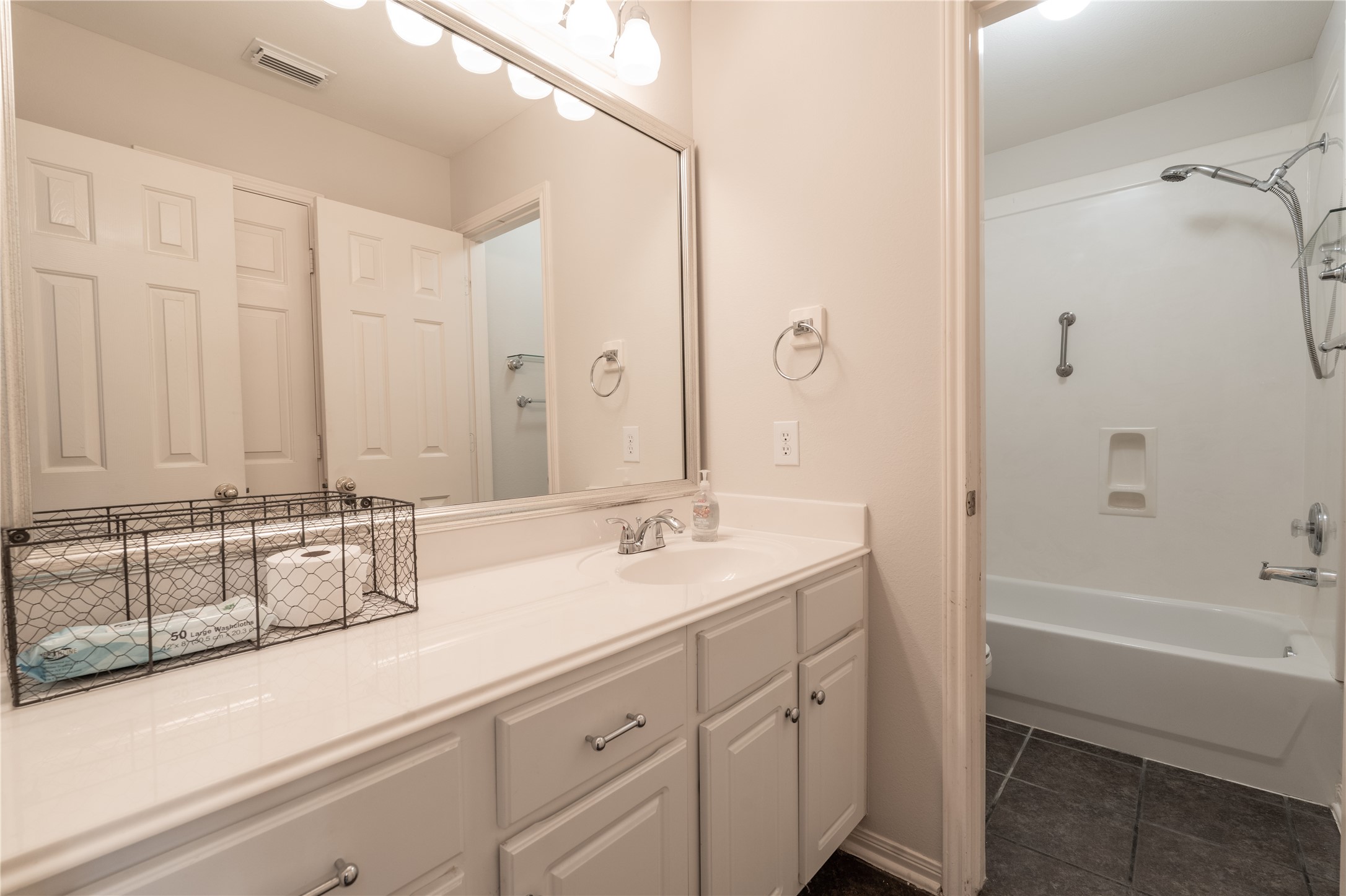 10619 Crownsedge Drive Spring, TX 77379 - Photo 16 of 38 This bathroom features a sleek double vanity with ample storage, a large mirror, and modern lighting. The space includes a full bathtub with a shower and neutral tile flooring, offering a clean and functional design.
