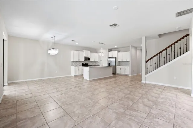 a view of an empty room with kitchen and window
