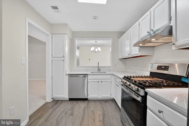 a kitchen with stainless steel appliances a sink dishwasher a stove and white cabinets with wooden floor