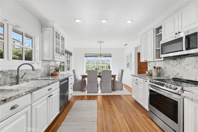 a large kitchen with stainless steel appliances granite countertop a stove top oven a sink dishwasher and white cabinets with wooden floor