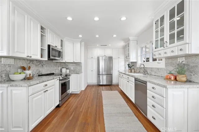 a kitchen with stainless steel appliances granite countertop a stove top oven a sink dishwasher and a refrigerator with wooden floor