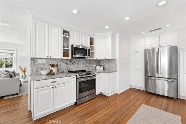 a kitchen with stainless steel appliances granite countertop a refrigerator stove a sink and white cabinets with wooden floor