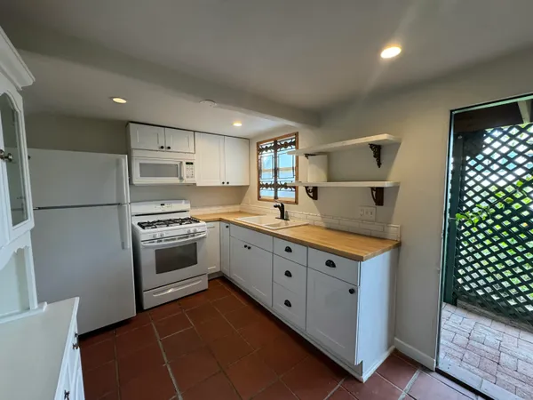 a large white kitchen with granite countertop a sink a stove a refrigerator and cabinets