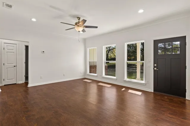 an empty room with wooden floor chandelier fan and windows