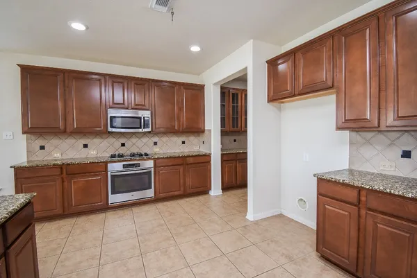 a kitchen with stainless steel appliances granite countertop a stove top oven a sink dishwasher and a refrigerator with wooden cabinets