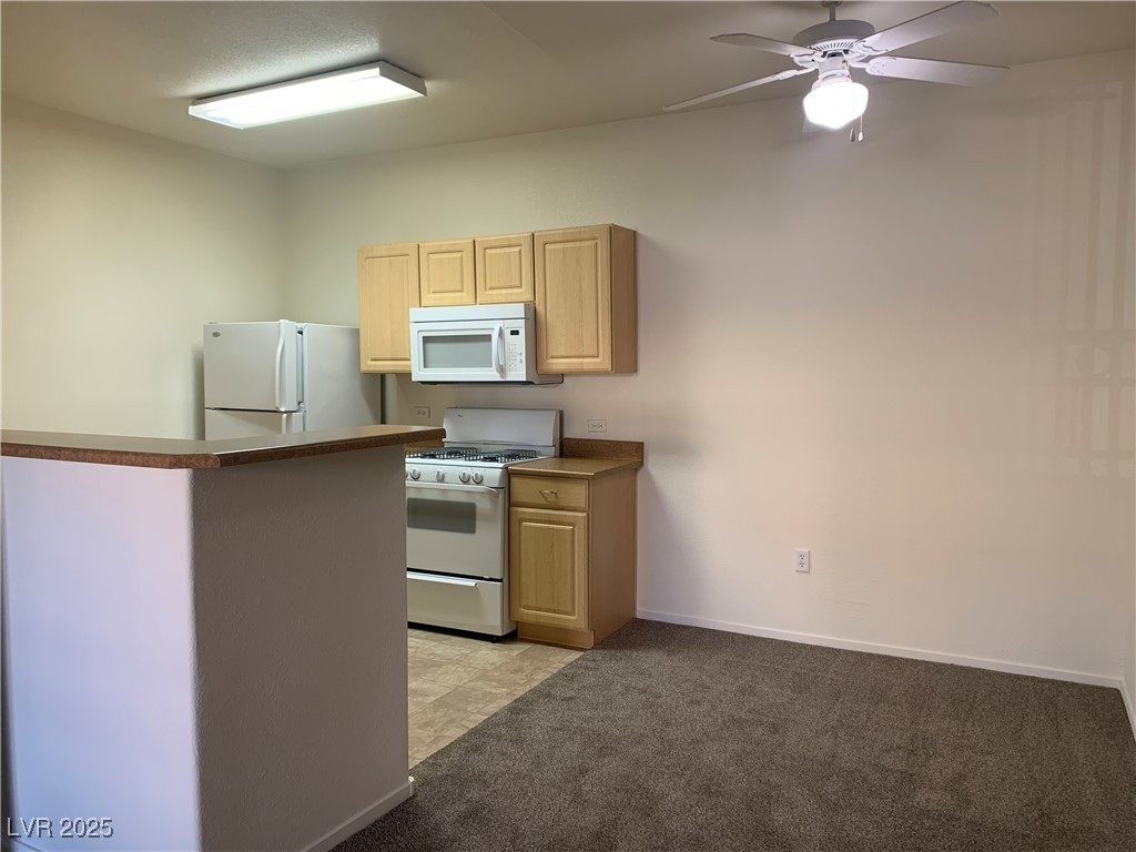 8250 North Grand Canyon Drive, Unit 1158 Las Vegas, NV 89166 - Photo 10 of 40 Kitchen with white appliances, light brown cabinets, light carpet, dark countertops, and a ceiling fan
