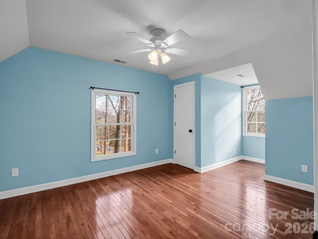 an empty room with wooden floor chandelier fan and windows
