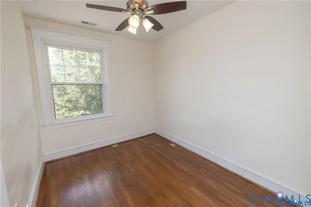 an empty room with wooden floor fan and windows