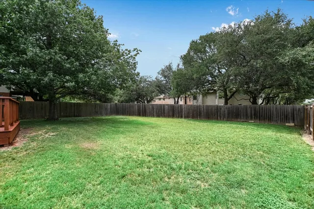 a view of a backyard with large trees and wooden fence