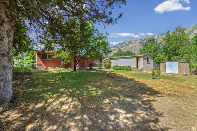 542 East 3400th Street North Provo, UT 84604 - Photo 28 of 39 Expansive backyard featuring mature trees, a red brick exterior, a concrete block auxiliary building, a wooden shed, and mountain scenery
