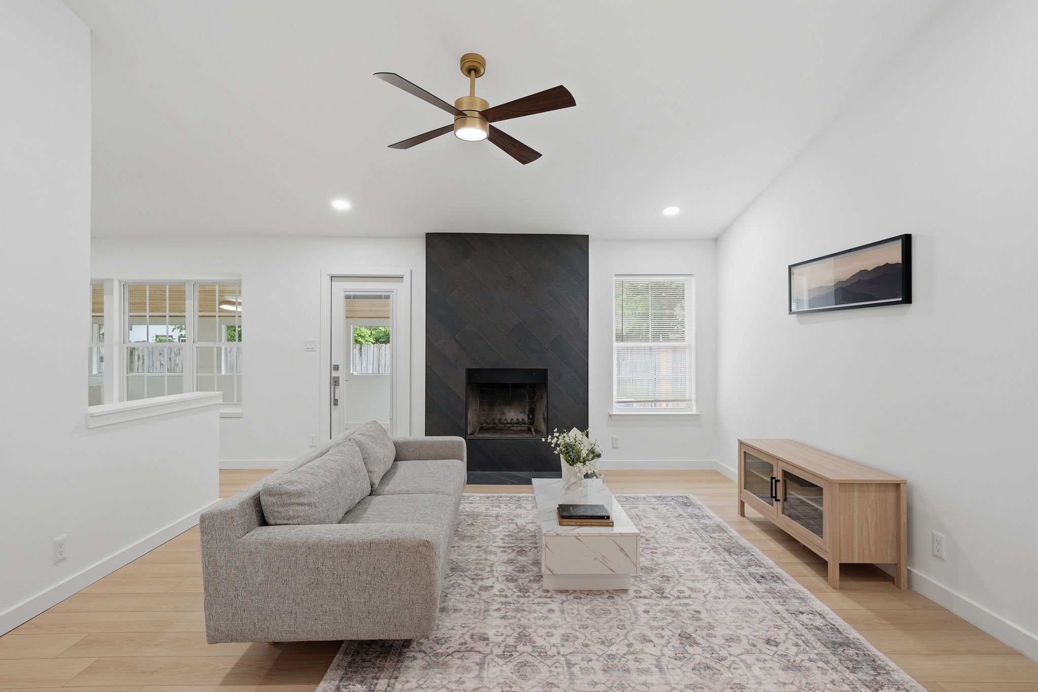 The living area features light wood flooring, a fireplace with a dark, textured surround, and recessed lighting