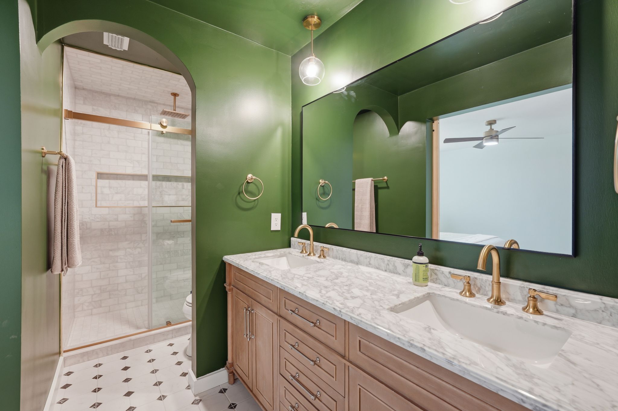 6804 Meadow Run Austin, TX 78745 - Photo 23 of 34 This bathroom features a double vanity with a marble countertop and gold-toned fixtures, a spacious shower with a glass enclosure and subway tile, and a decorative arched entryway