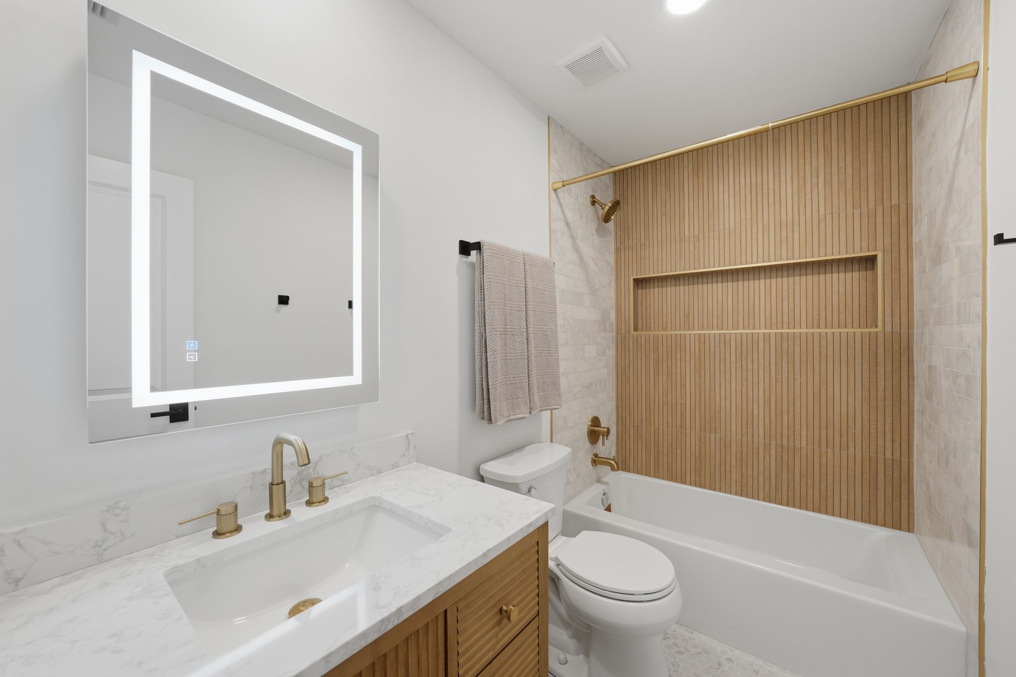 6804 Meadow Run Austin, TX 78745 - Photo 25 of 34 Bathroom featuring a vanity with a white countertop and gold fixtures, an illuminated mirror, and a bathtub with a tiled surround
