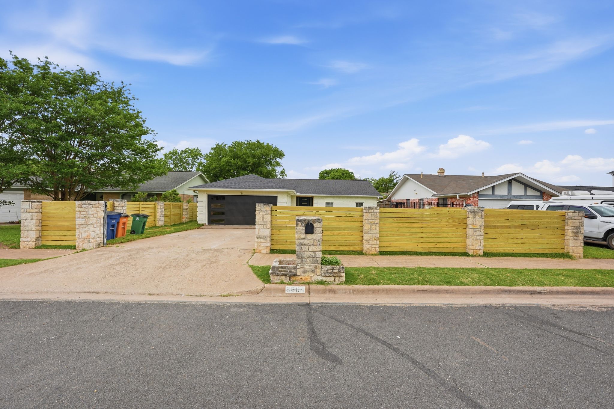 6804 Meadow Run Austin, TX 78745 - Photo 3 of 34 The property features a stone and wood fence, a paved driveway, and a front lawn with mature trees