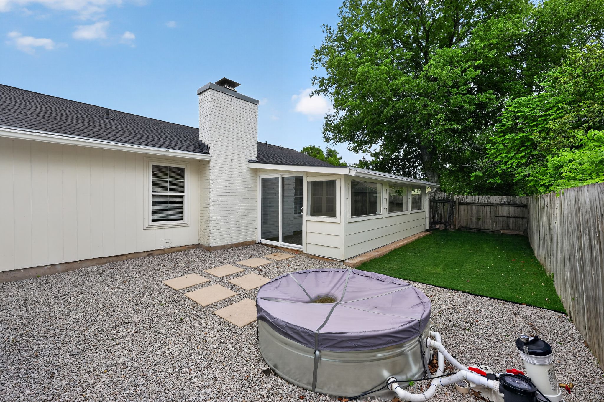 6804 Meadow Run Austin, TX 78745 - Photo 31 of 34 The property features a white brick chimney, a sunroom with sliding glass doors and windows, and a backyard with a gravel area, stepping stones, and a patch of green lawn