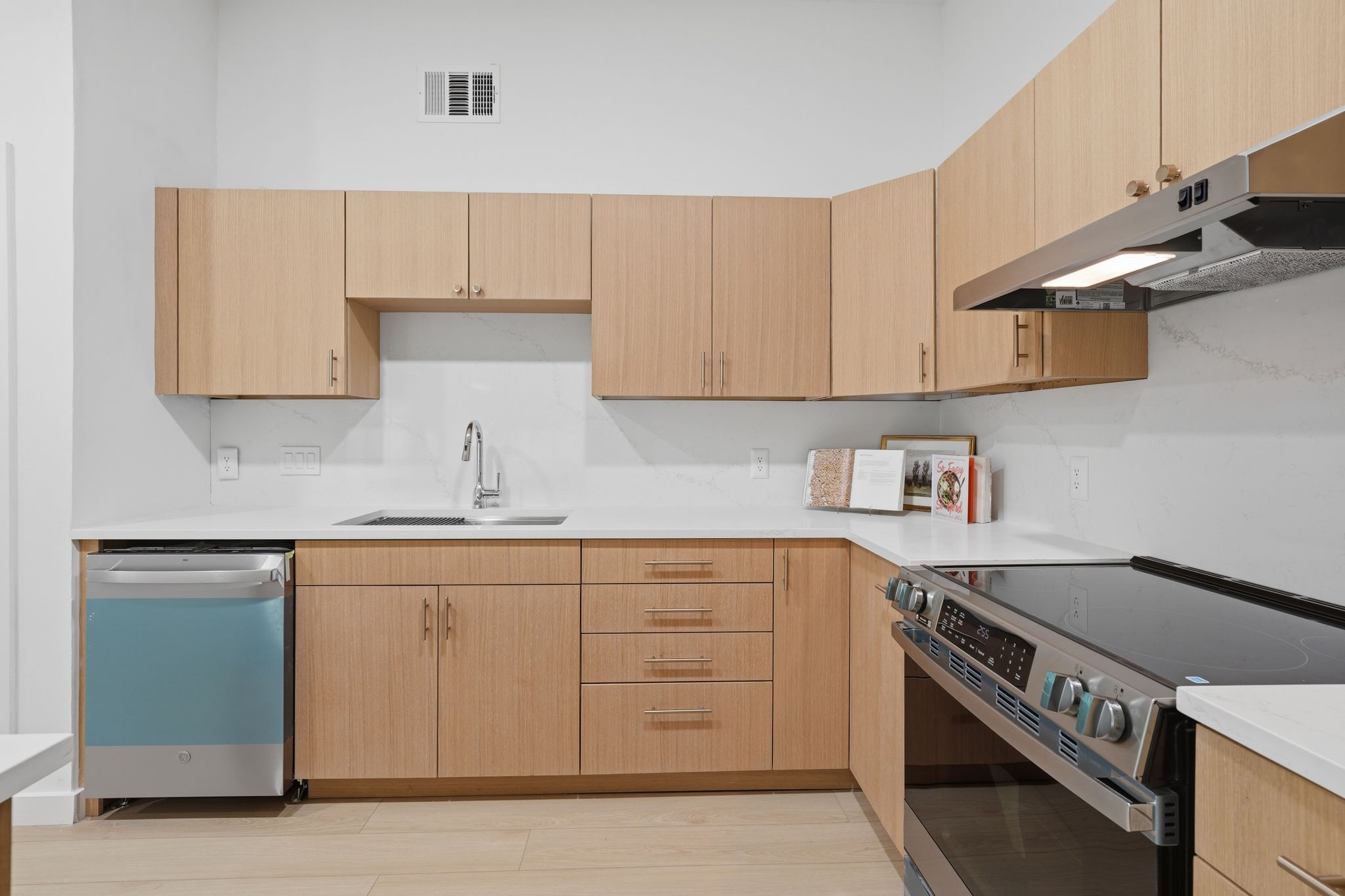 6804 Meadow Run Austin, TX 78745 - Photo 10 of 34 The kitchen features wooden cabinetry, white countertops, a stainless steel dishwasher, and an electric range with an overhead vent