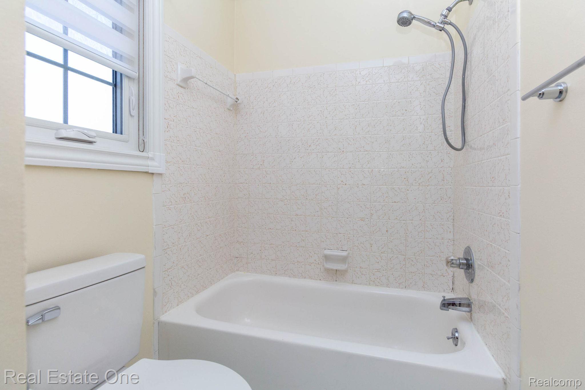 111 Manor Way Rochester, MI 48309 - Photo 24 of 36 White porcelain bathtub with a textured tile surround, chrome fixtures, and an adjacent window with horizontal blinds