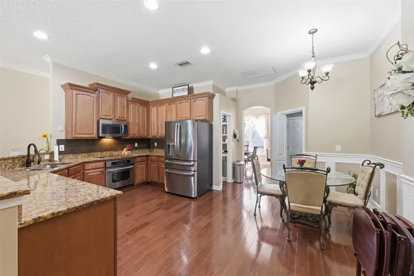 a kitchen with stainless steel appliances granite countertop a refrigerator a stove top oven a sink dishwasher a dining table and chairs with wooden floor