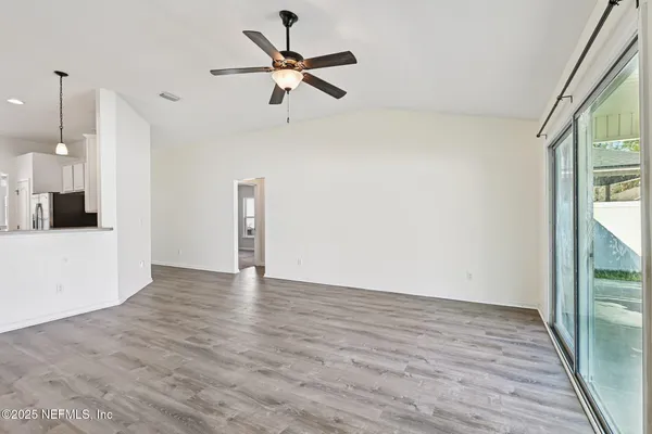 a view of a livingroom with wooden floor a ceiling fan and windows