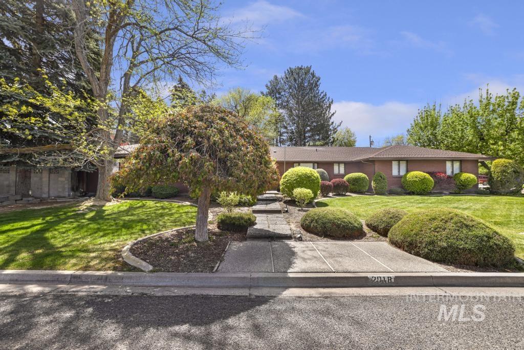2018 Rancho Vista Drive Twin Falls, ID 83301 - Photo 4 of 50 Single-story brick exterior residence featuring a low-pitched roof, front lawn with mature trees, and sculpted shrubbery landscaping