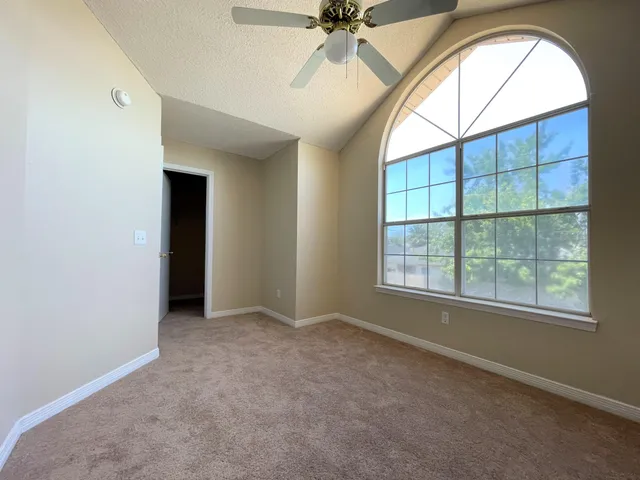an empty room with chandelier fan and windows
