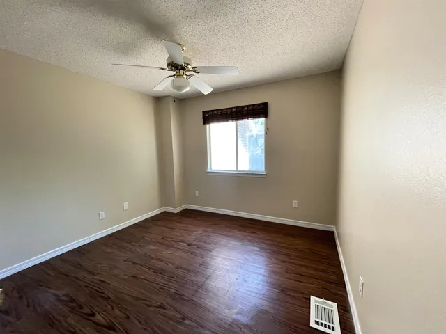 an empty room with wooden floor chandelier fan and windows