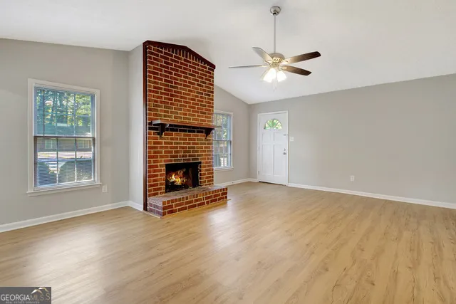 a view of an empty room with wooden floor fireplace and a window