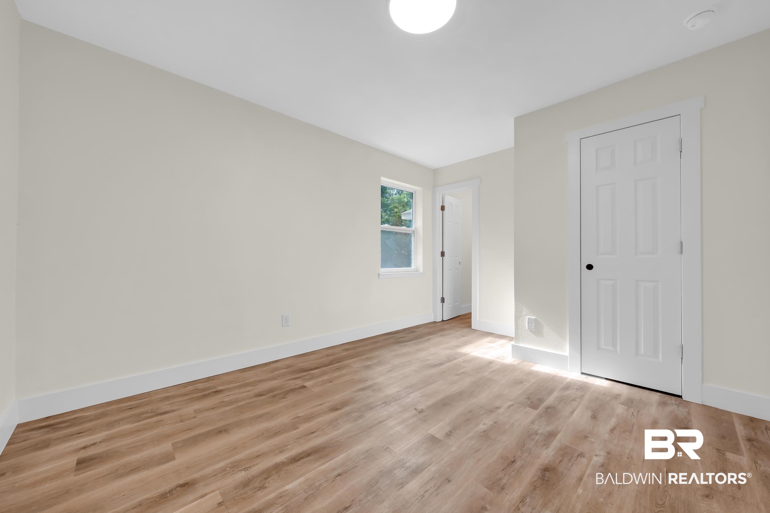 5109 McDonald Road Theodore, AL 36582 - Photo 17 of 21 Room featuring wood-finish flooring, white baseboards, a white six-panel door with black hardware, a single window, and a flush-mount ceiling light fixture